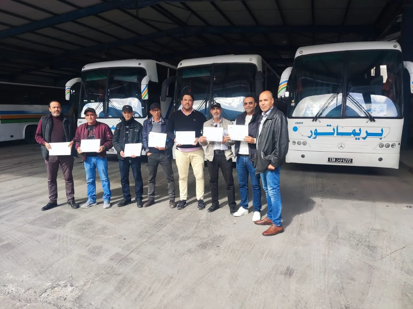 Groupe de chauffeurs tenant leur attestation devant des autocars